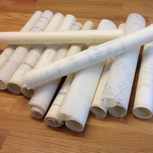 Zusammengerollte Grundrisspläne, die leicht duchsichtig sind. Zu erkennen sind Grundrisse auf dem pergamentartigem Papier.